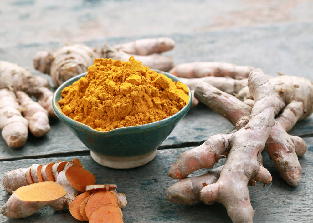 Turmeric powder in bowl next to roots