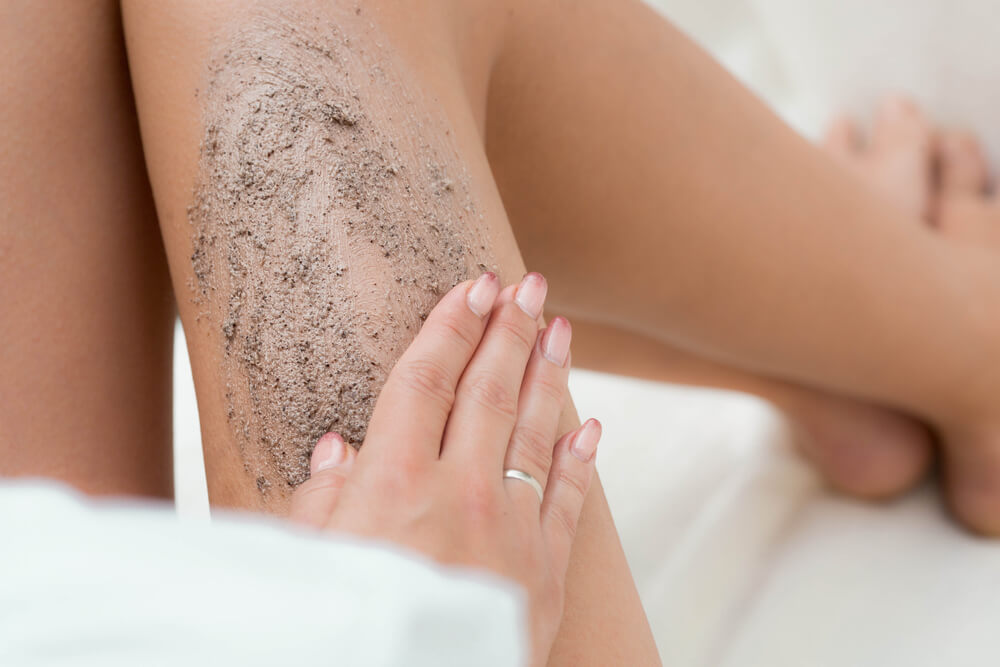 Woman using body scrubs on legs